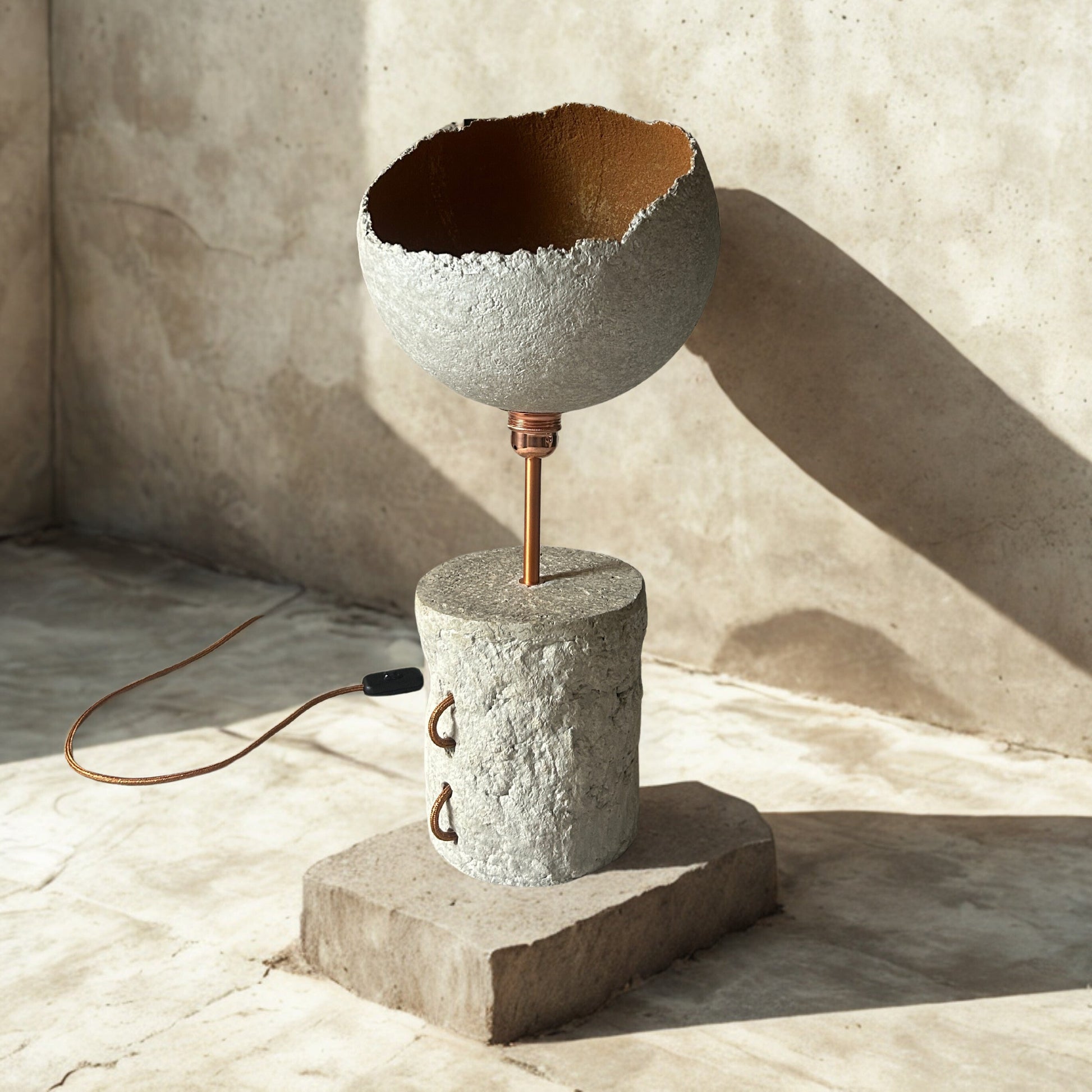 Ceramic lamp with textured design on a concrete base against a textured wall.