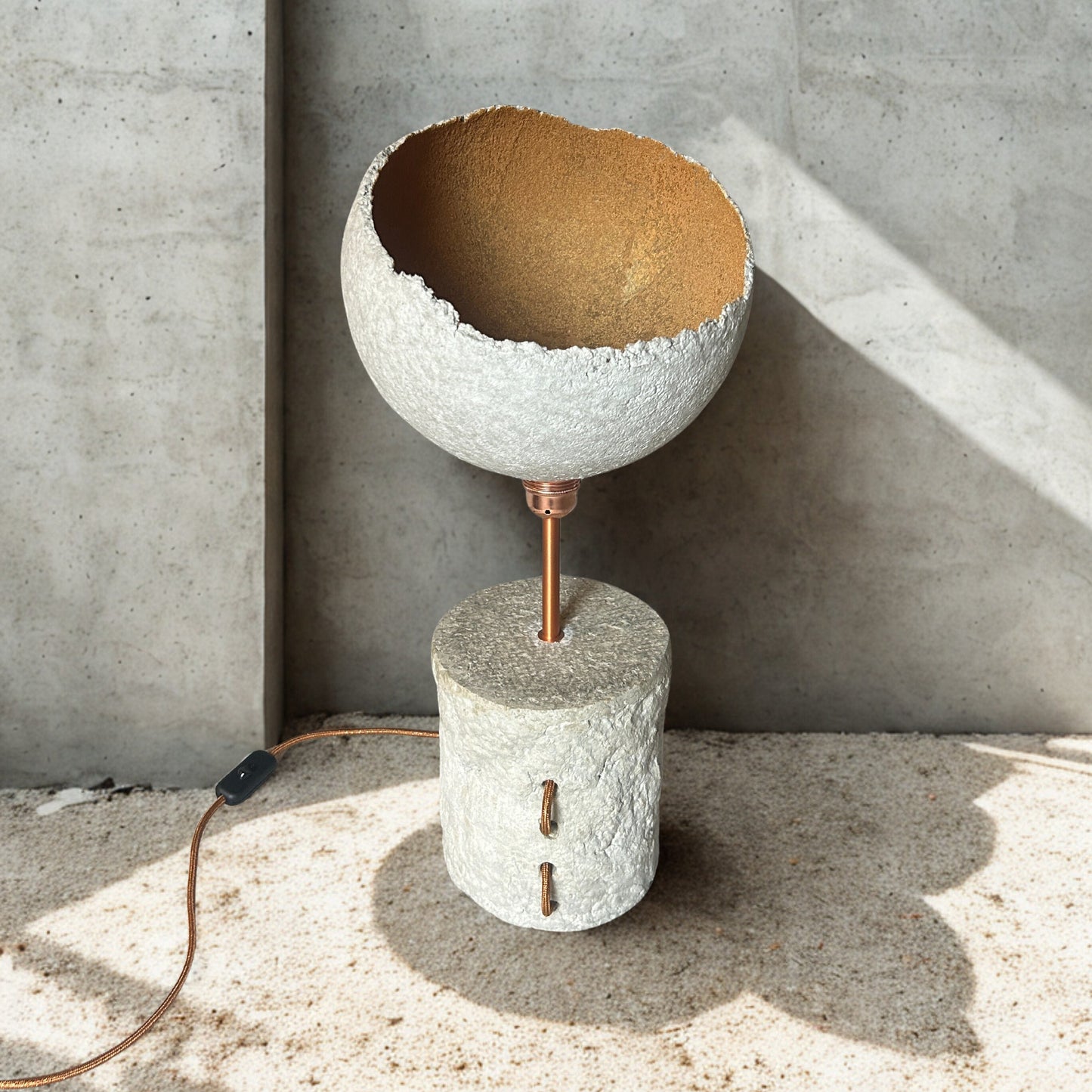 Concrete lamp with a brown interior against a concrete wall