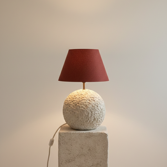 Decorative lamp with a textured base and red shade on a light gray background