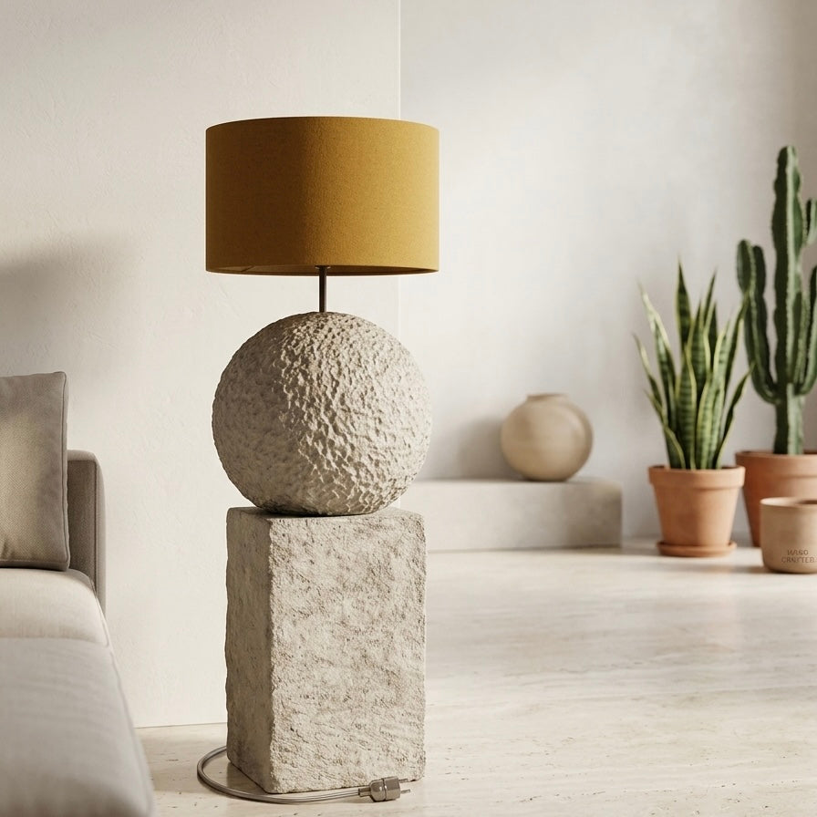 Decorative lamp with textured base and gold shade in a room with plants and a bed.