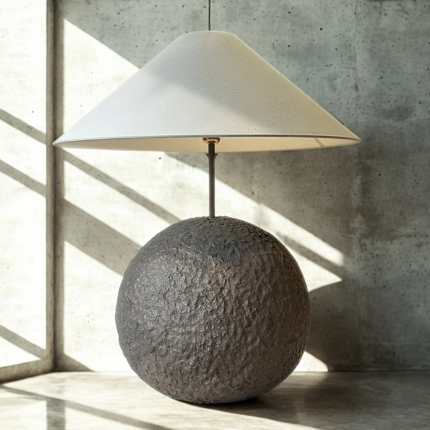 Table lamp with a textured spherical base and white conical shade on a concrete floor.