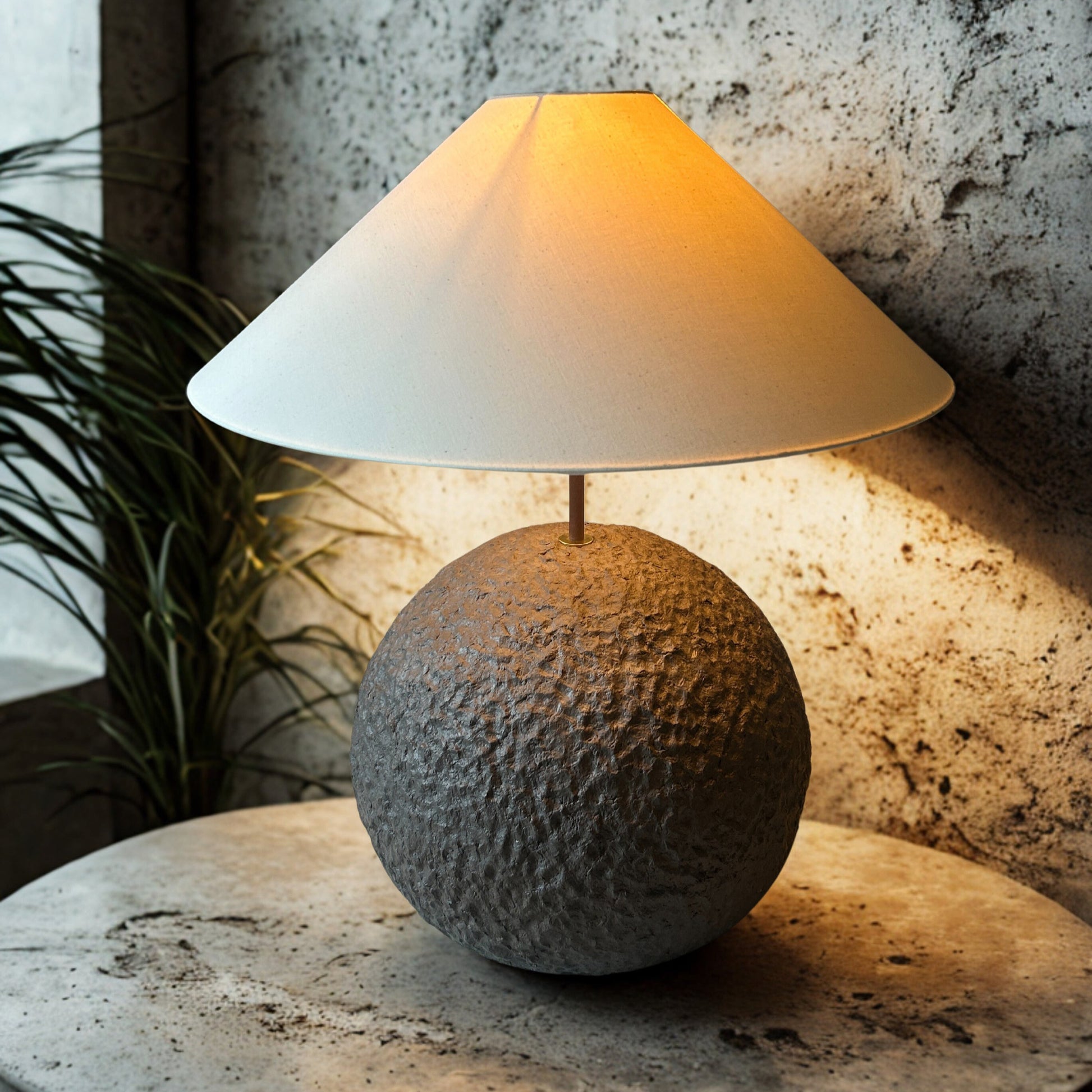Table lamp with textured base and white shade on a stone surface against a textured wall.