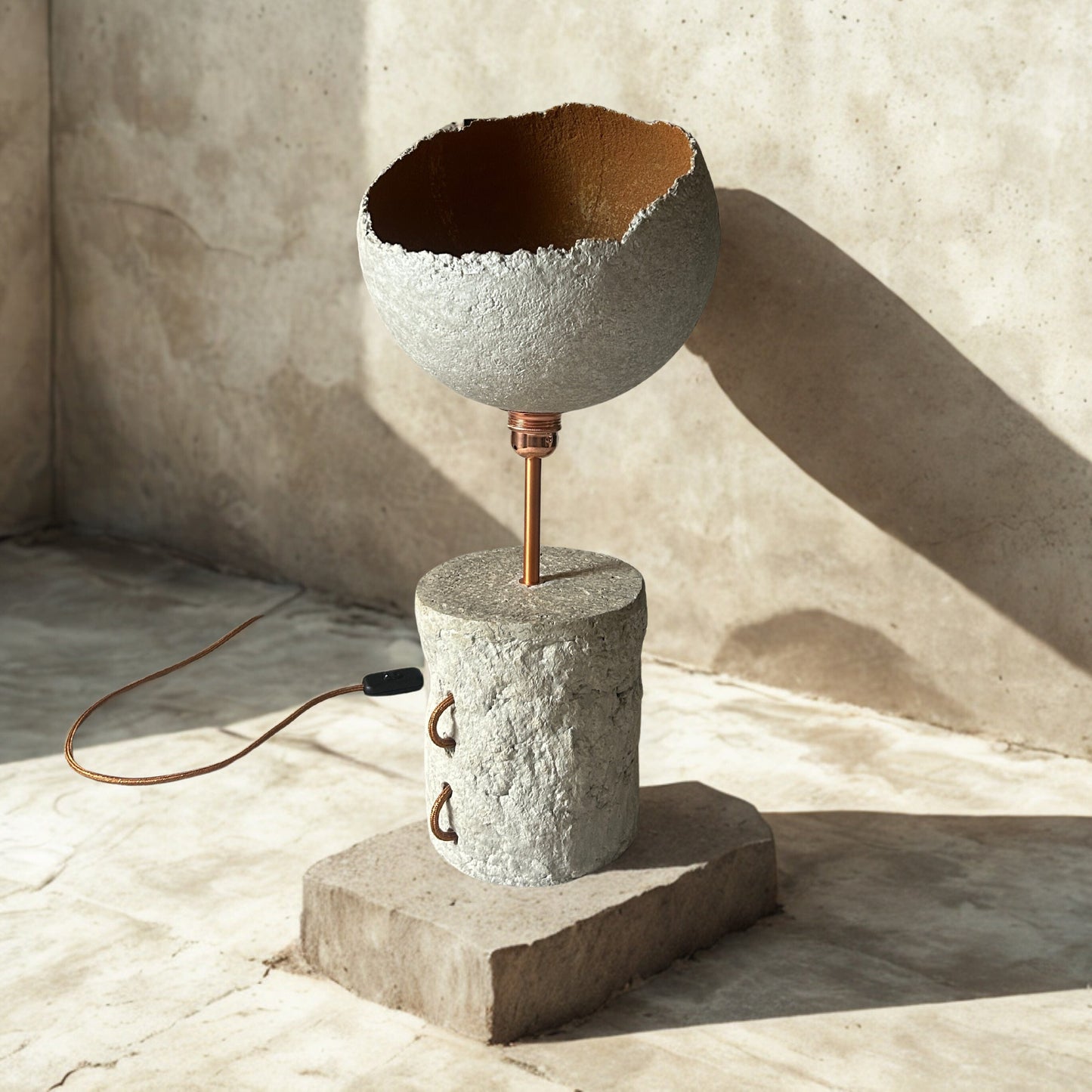 Ceramic lamp with textured design on a concrete base against a textured wall.