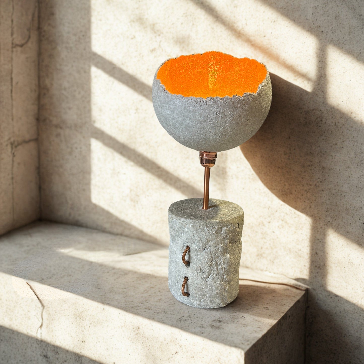 Concrete lamp with orange interior on a concrete surface with sunlight casting shadows